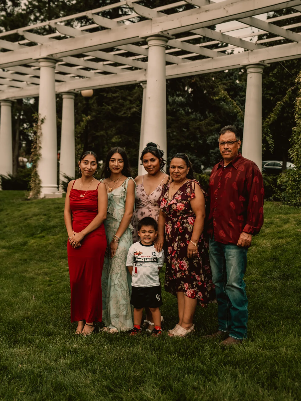 The family standing together on the lawn beneath a white garden pergola