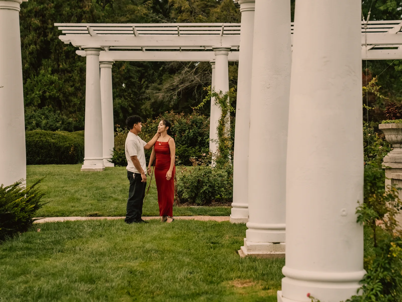 The couple standing between the white pergola columns
