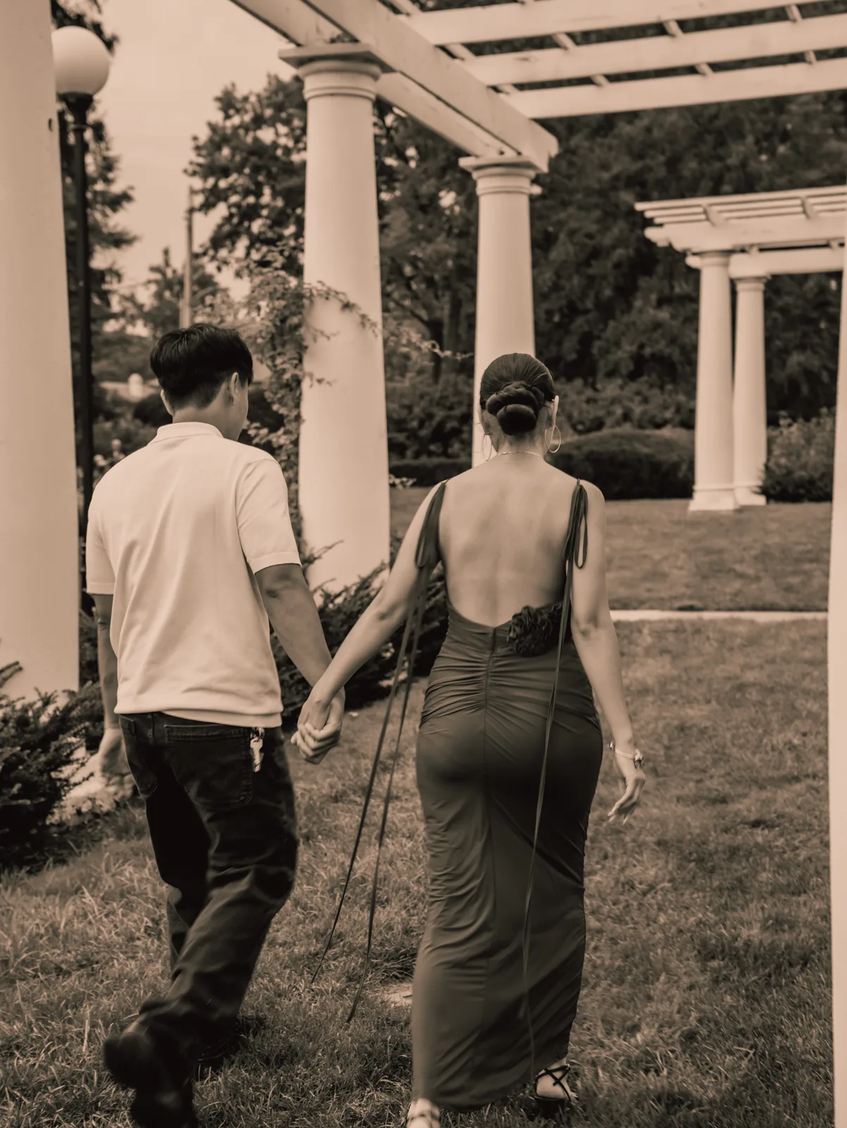 The couple walking hand in hand beneath the pergola, toned