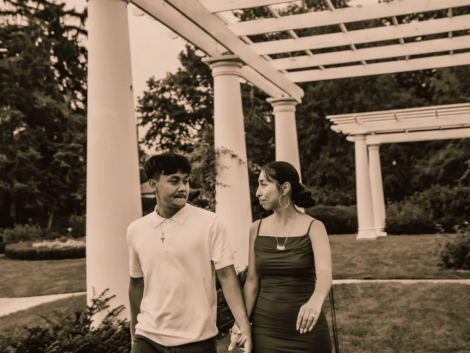 The couple standing side by side beneath the pergola