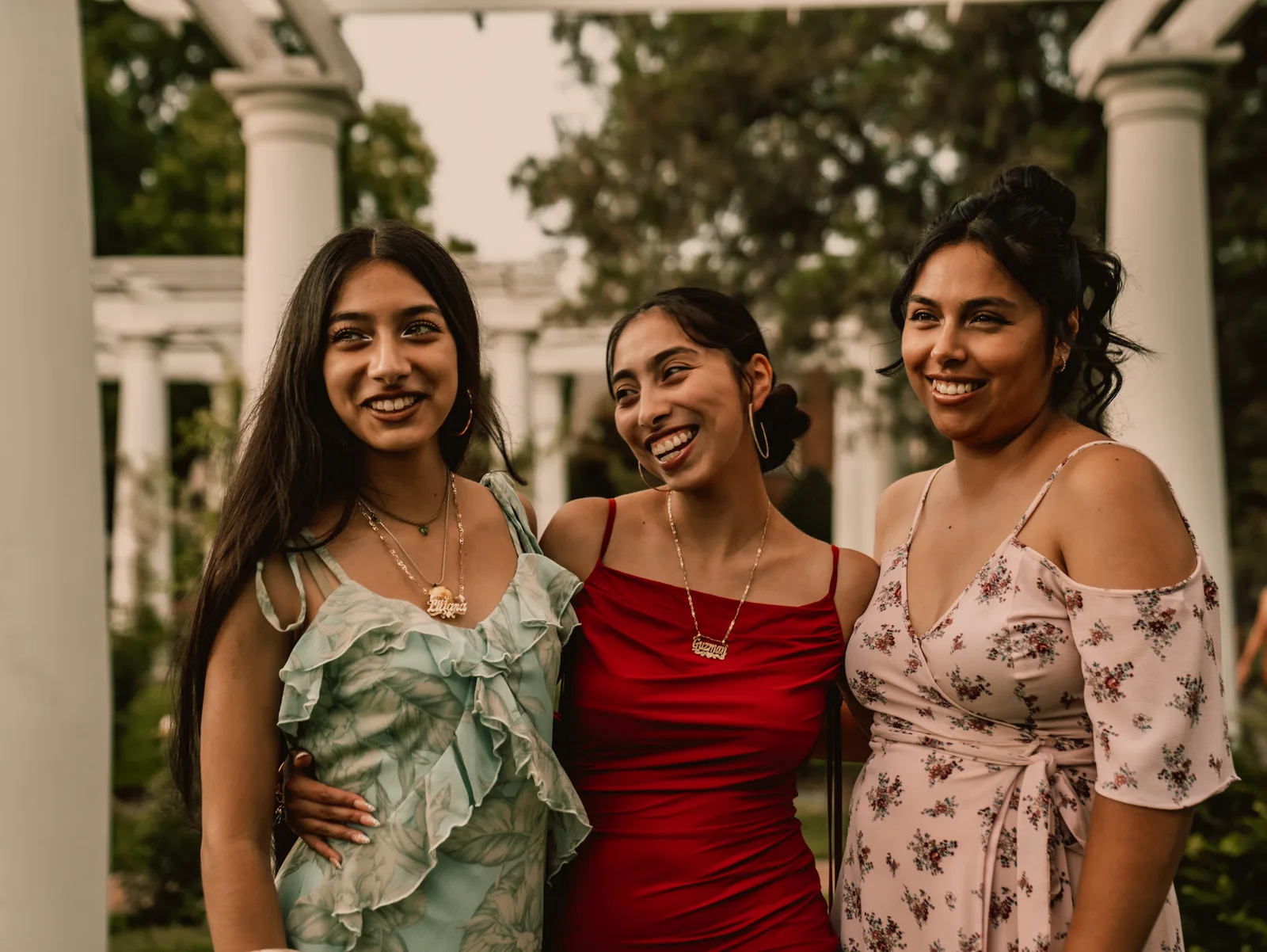 Three sisters smiling together beneath the pergola