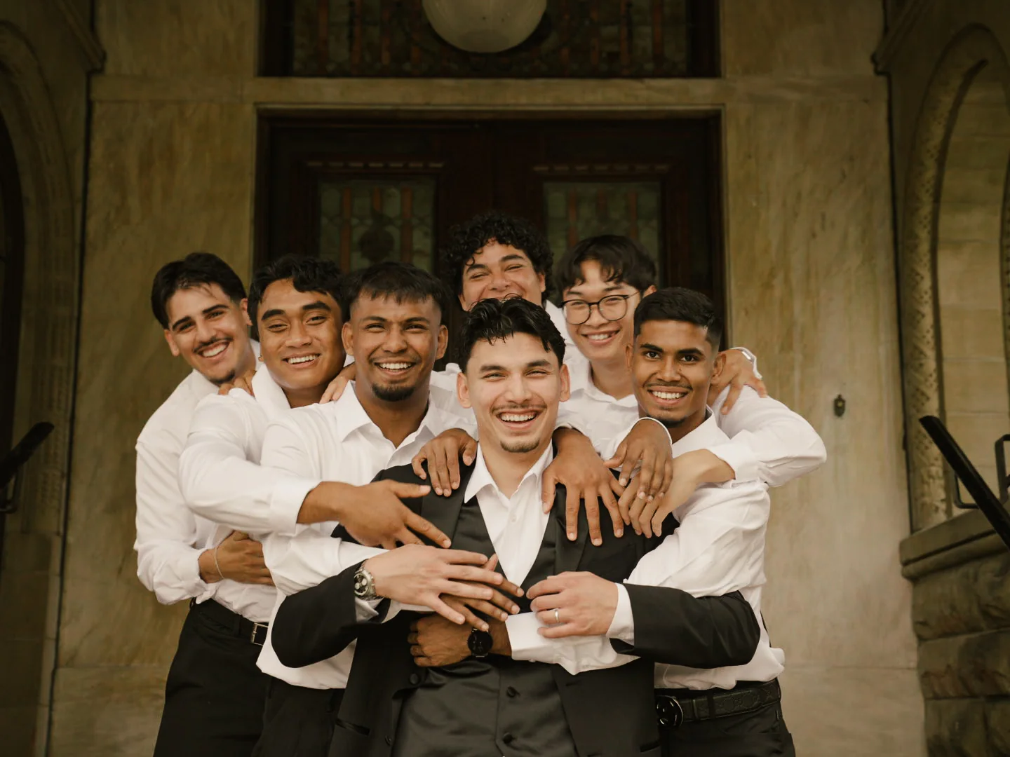 The groom laughing with his wedding party outside a stone building